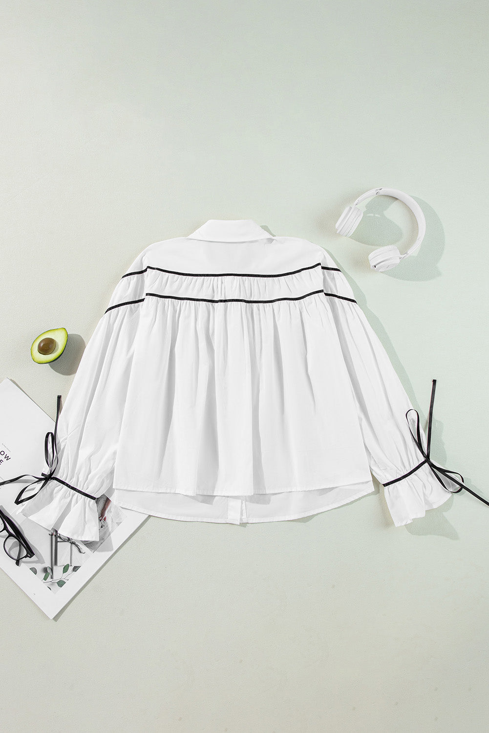 White blouse with black piped trim and bow details on ruffled cuffs.
