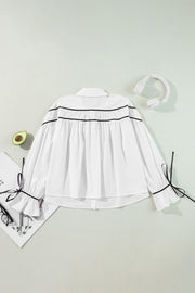 White blouse with black piped trim and bow details on ruffled cuffs.