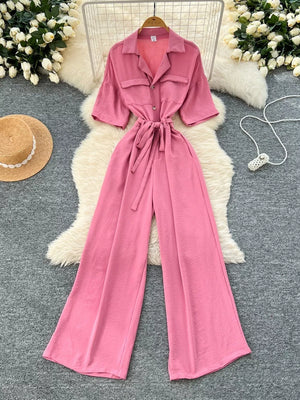 Pink belted wide-leg jumpsuit with pockets and buttoned front, short sleeves.