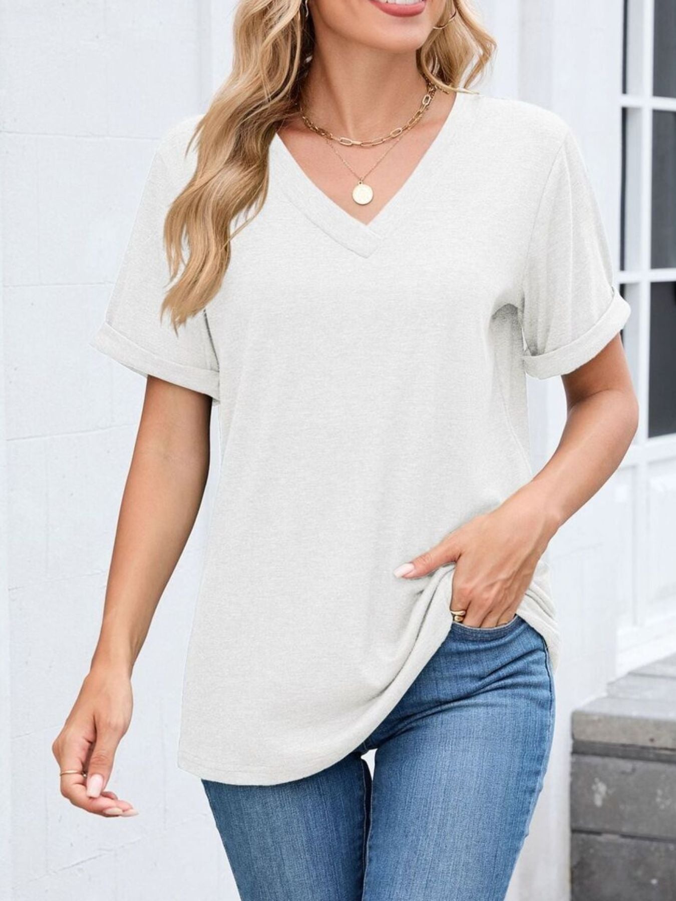 White v-neck t-shirt with cuffed short sleeves and a relaxed fit, styled with jeans.