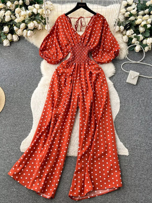 Scarlet polka dot smocked wide-leg romper with V-neck and puff sleeves.