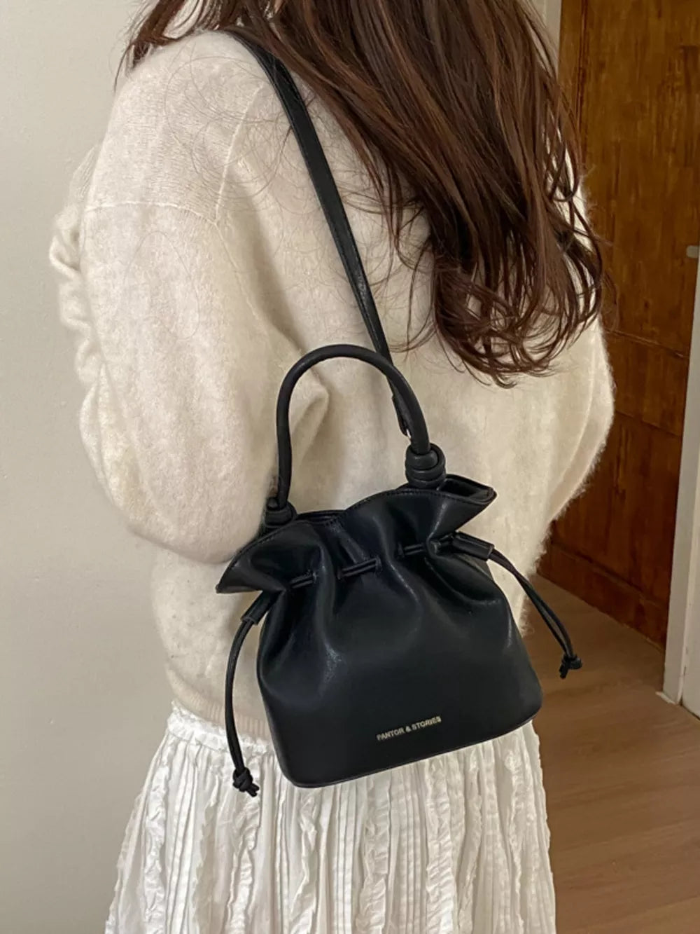 Black pu leather cinch-top crossbody bag with drawstring and knotted handle detail.
