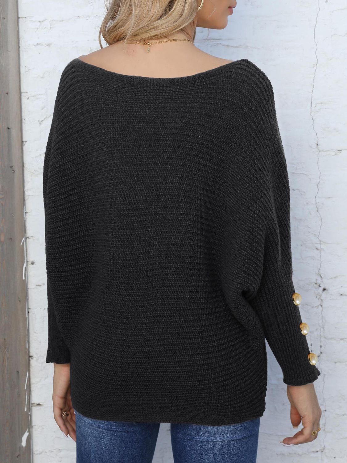 Black batwing knit sweater with boat neck and pearl button cuff detail.