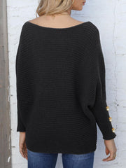 Black batwing knit sweater with boat neck and pearl button cuff detail.