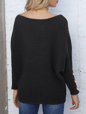 Black batwing knit sweater with boat neck and pearl button cuff detail.