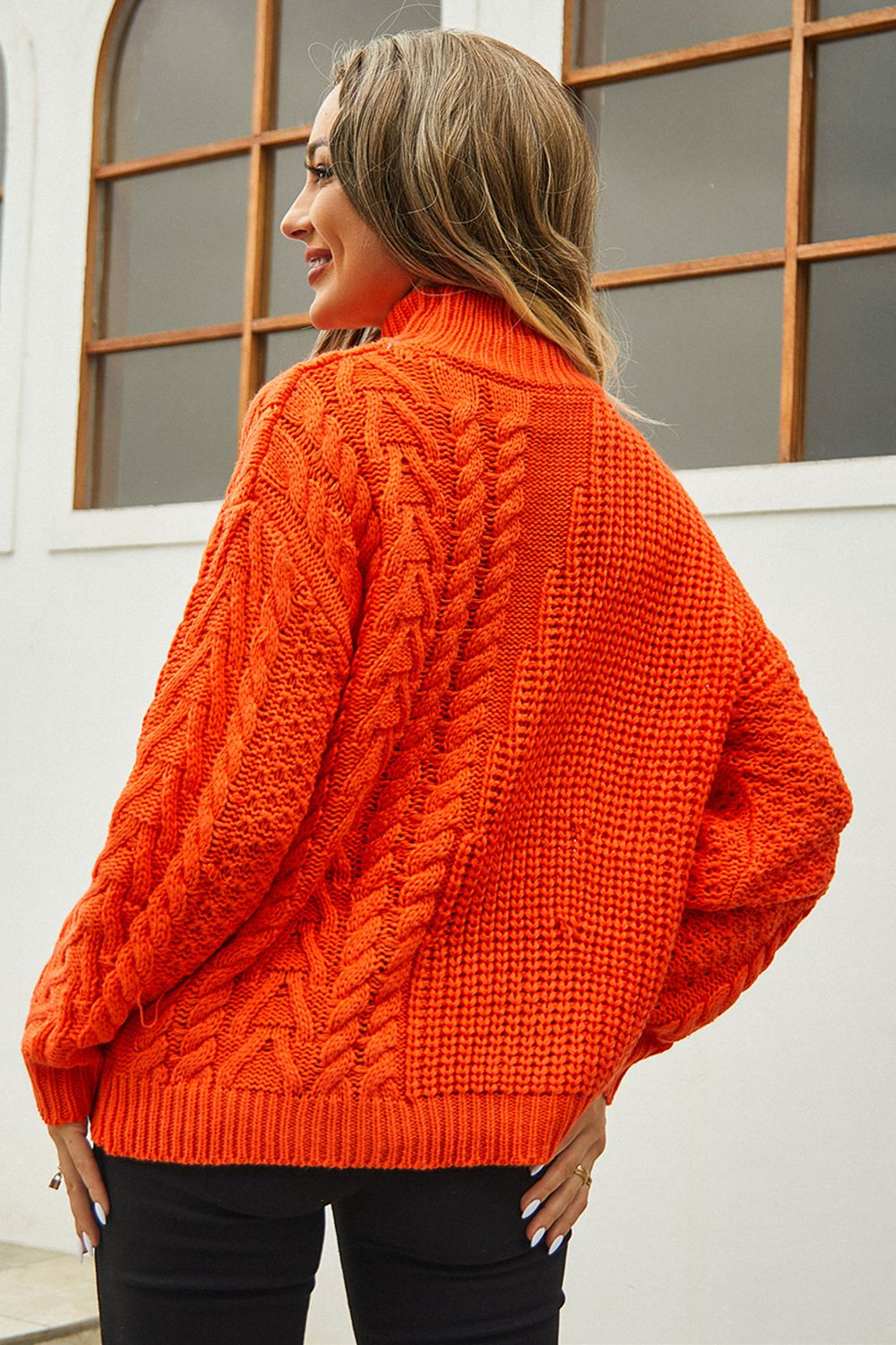 Orange cable-knit turtleneck sweater with voluminous silhouette and textured acrylic knit.