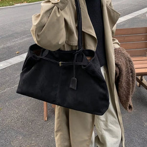 Black suede slouchy shoulder bag with drawstring and gold hardware detail.