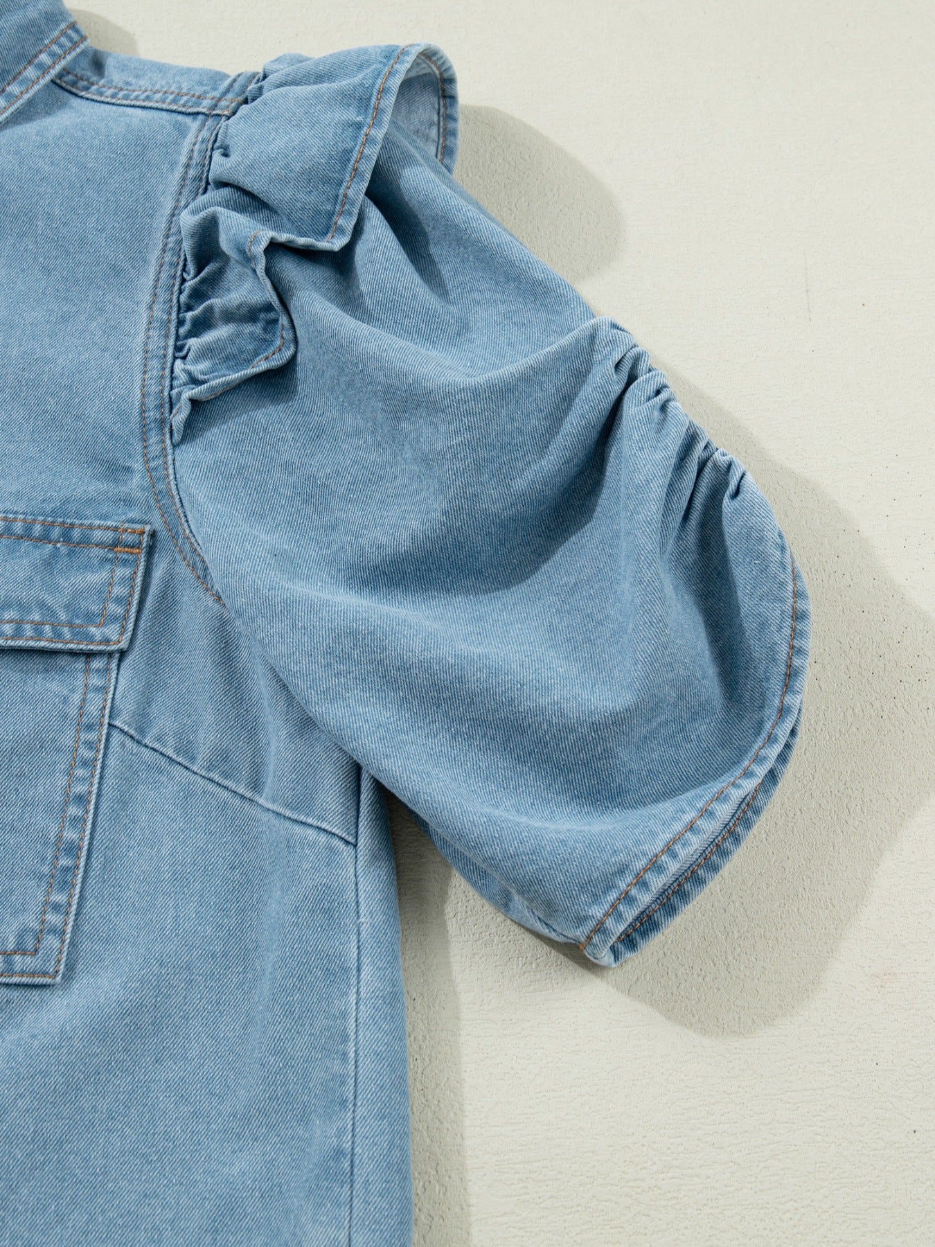 Light wash denim shirt with ruffled short sleeves and ruched cuffs.