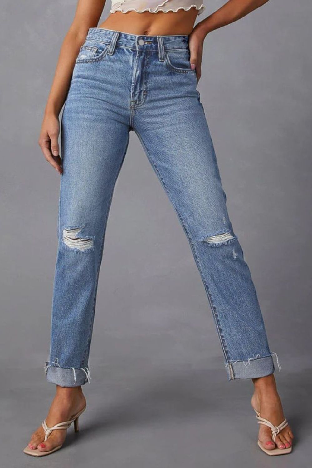Distressed straight leg jeans in medium wash denim with ripped knees and cuffed hems.