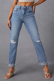 Distressed straight leg jeans in medium wash denim with ripped knees and cuffed hems.