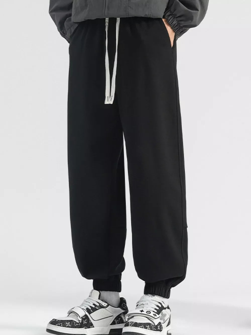 Men's black loose fit sweatpants with white drawstring and cuffed ankles.