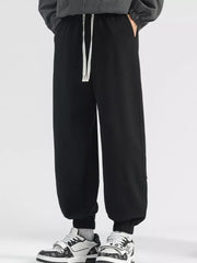 Men's black loose fit sweatpants with white drawstring and cuffed ankles.