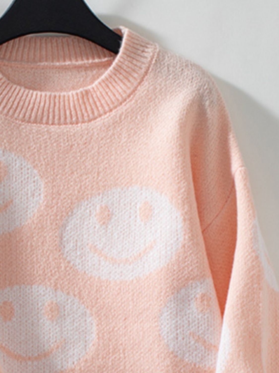 Watermelon pink knit sweater with allover white smiley face intarsia pattern and crewneck.