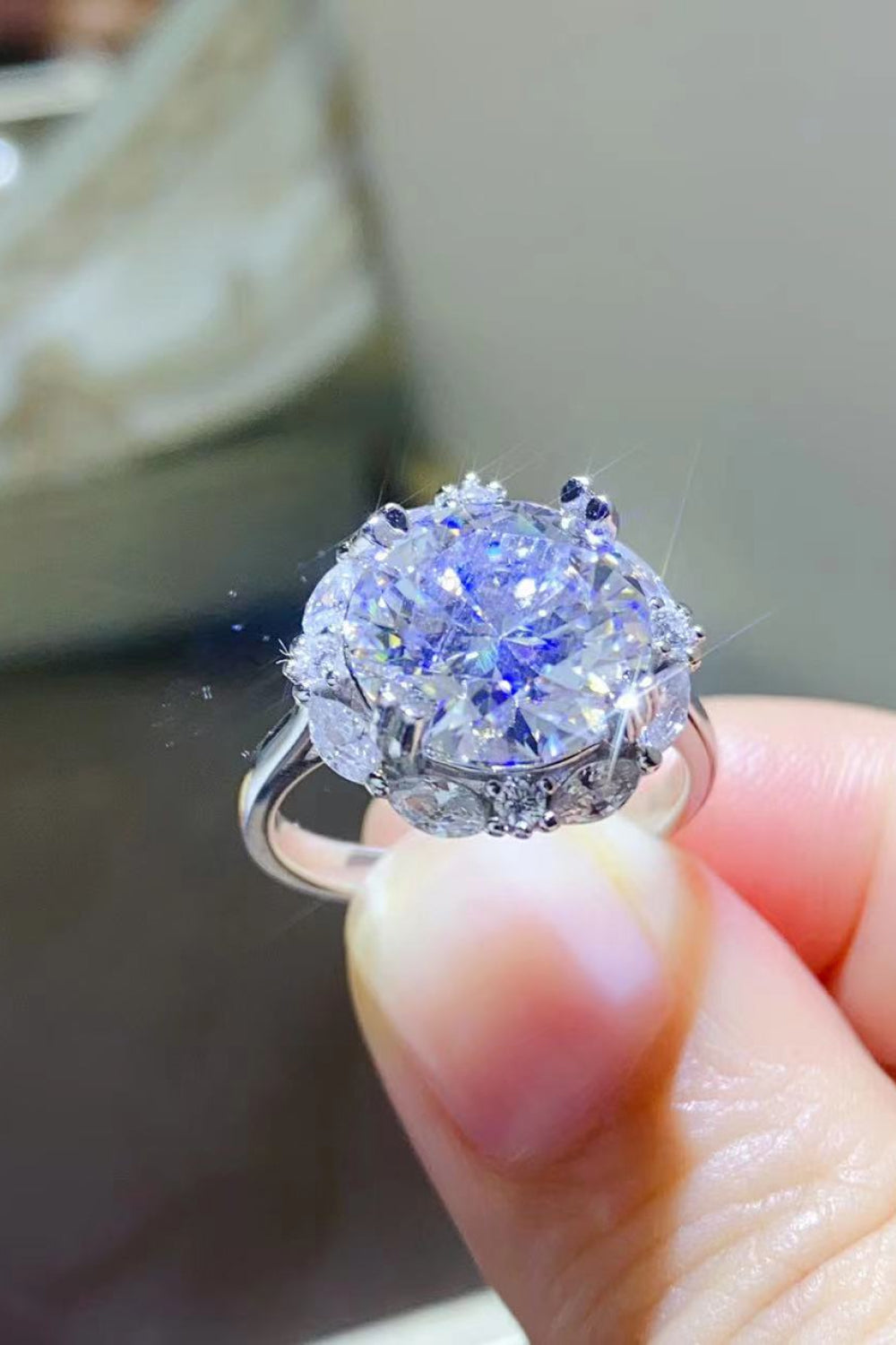 Silver moissanite halo ring with large center stone and smaller accent stones.