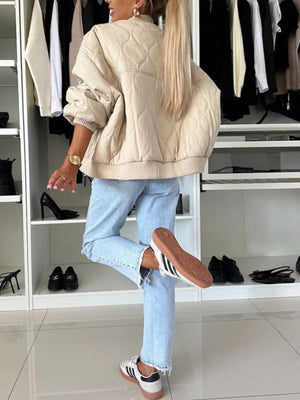 Beige quilted bomber jacket with rounded sleeves and ribbed cuffs, styled with light wash jeans.