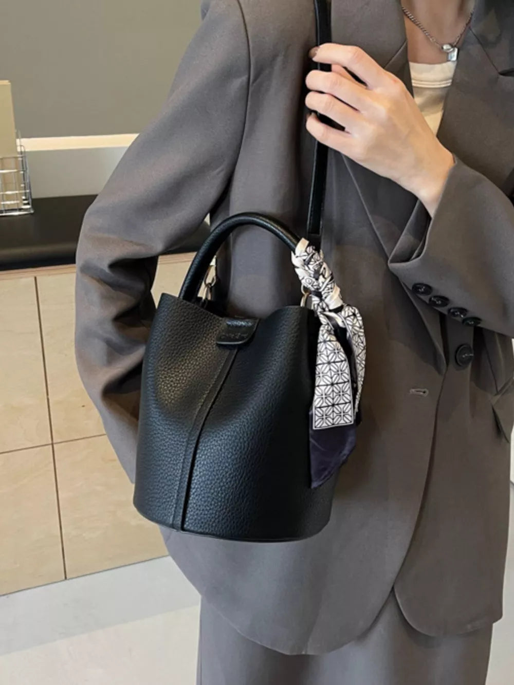 Black pebbled leather bucket bag with scarf detail and top handles.