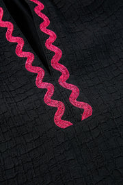 Black blouse with textured fabric and pink embroidered zigzag neckline detail.