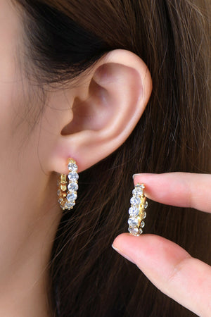 Gold moissanite pavé hoop earrings with clear stones, shown on ear and held by fingers.