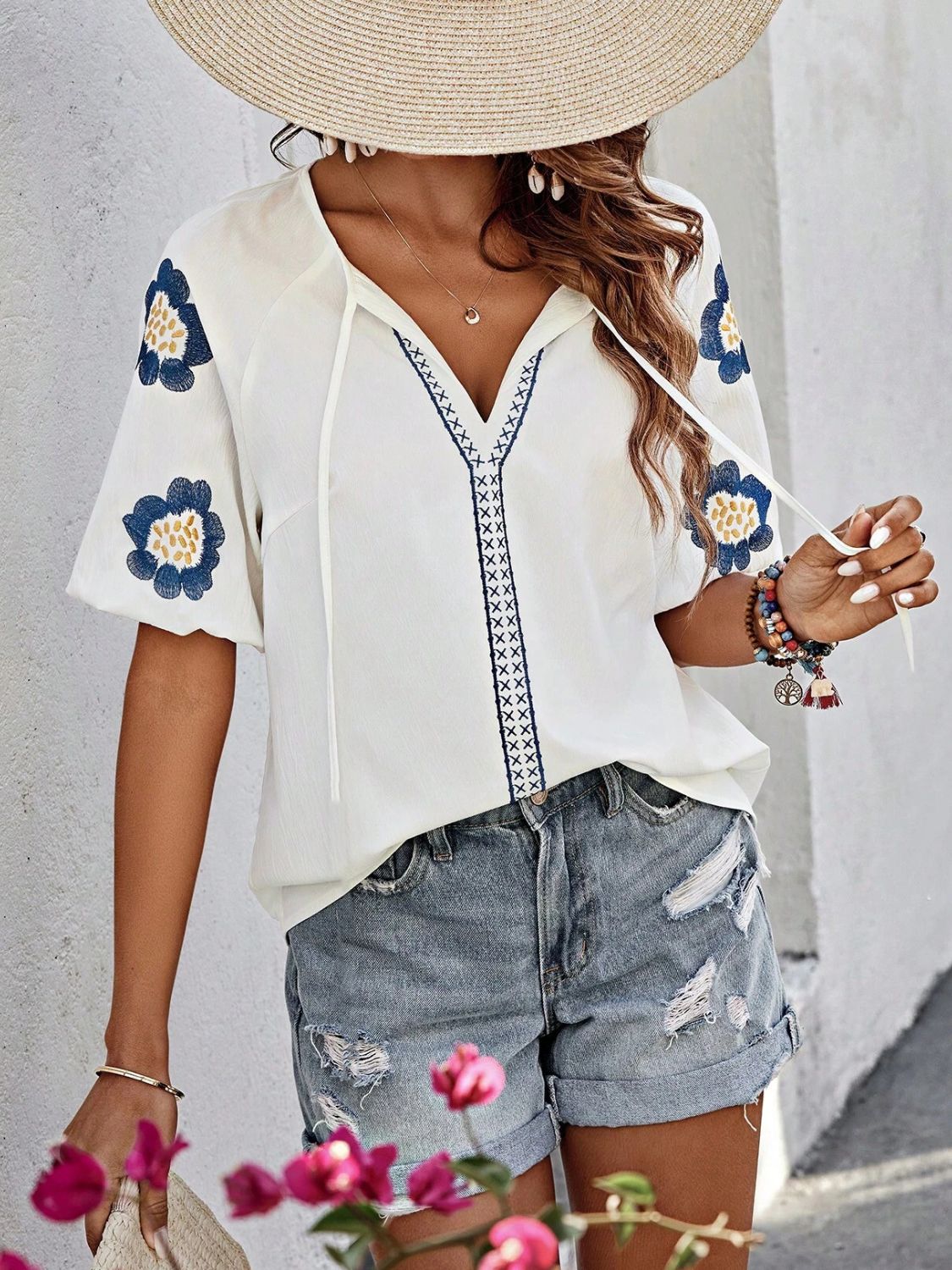 White embroidered yoke sleeve blouse with blue floral details and tie neck.