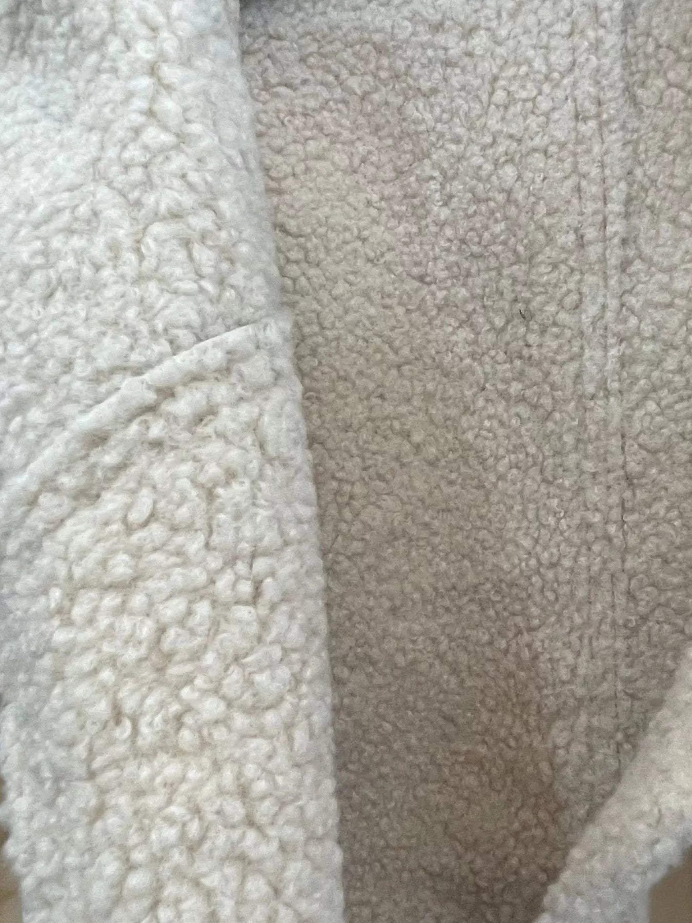 Cropped sherpa jacket in beige with fuzzy texture and pocket detail.