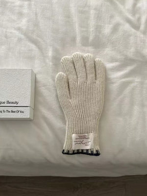 Ivory ribbed knit gloves with a dark blue scalloped cuff detail and a decorative label.
