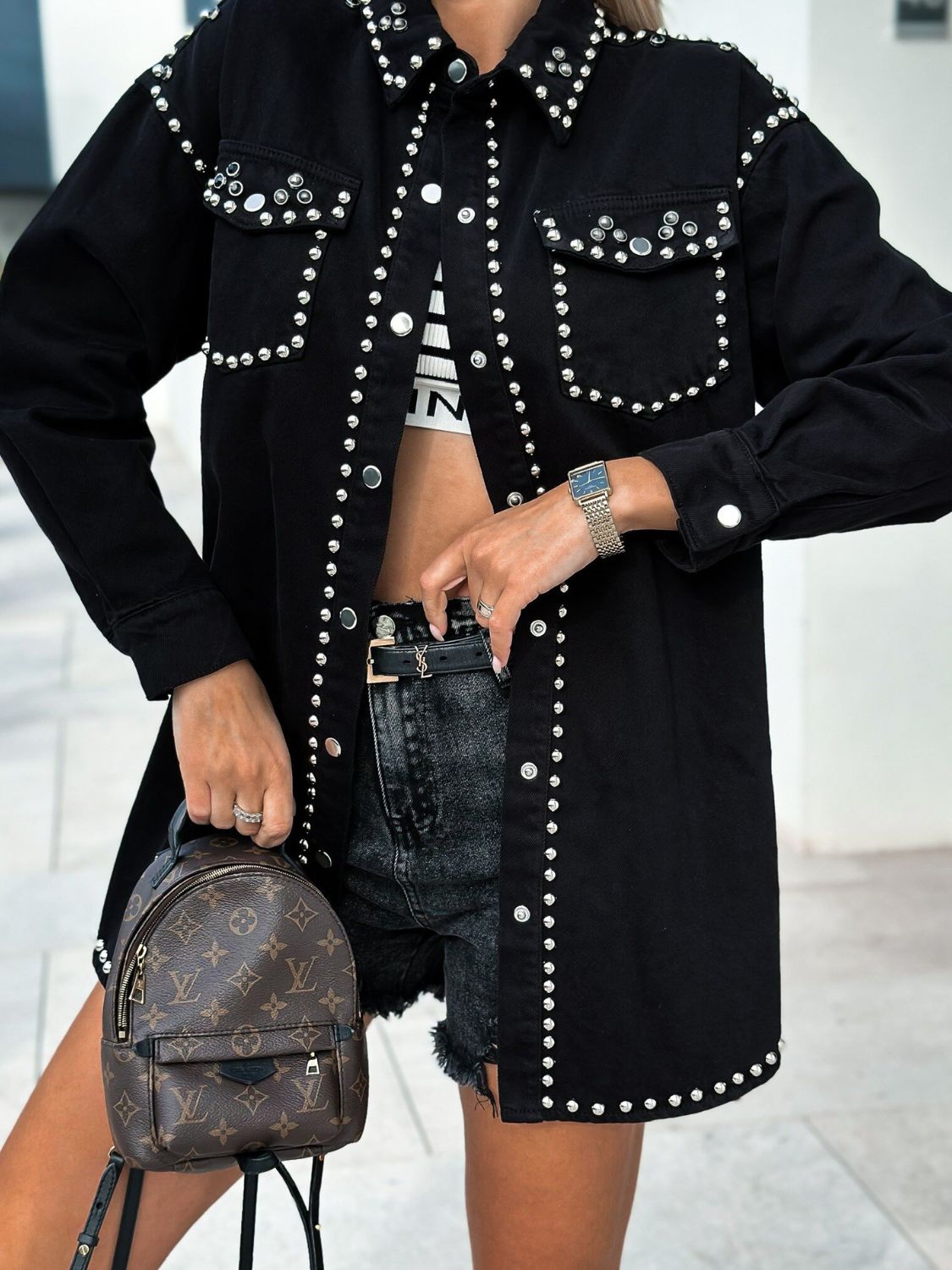 Black studded denim shirtdress with a belted waist, worn with denim shorts.