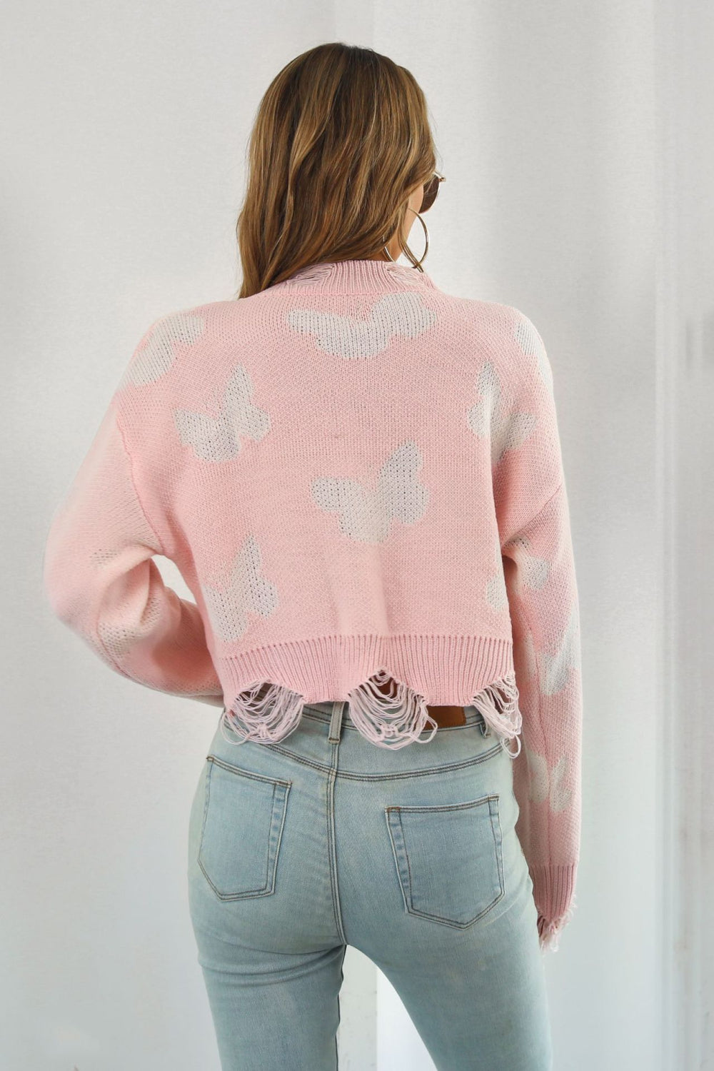 Pink acrylic knit cropped sweater with butterfly intarsia and frayed hem
