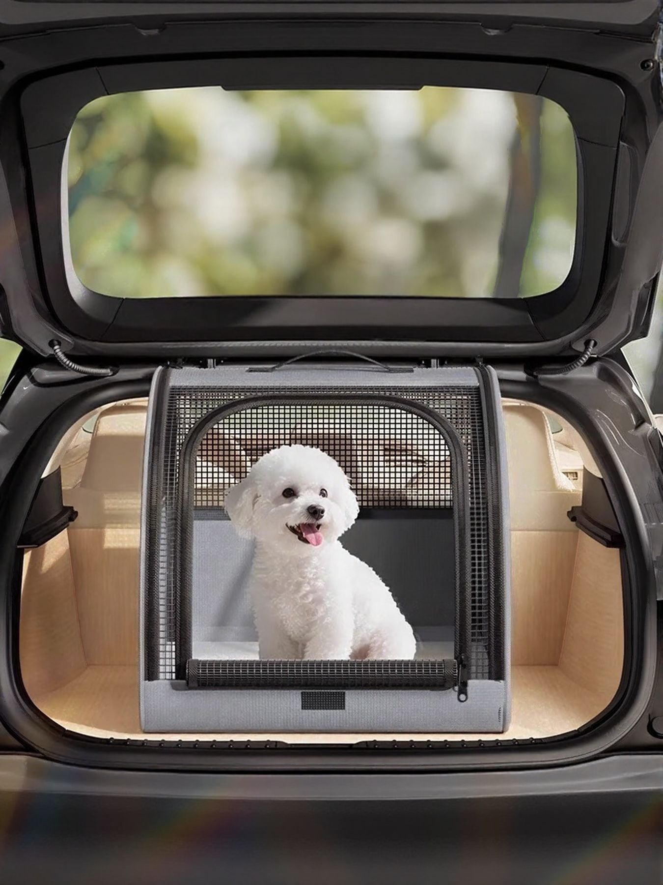 Gray pet carrier with mesh windows and a white dog inside, placed in a car trunk.