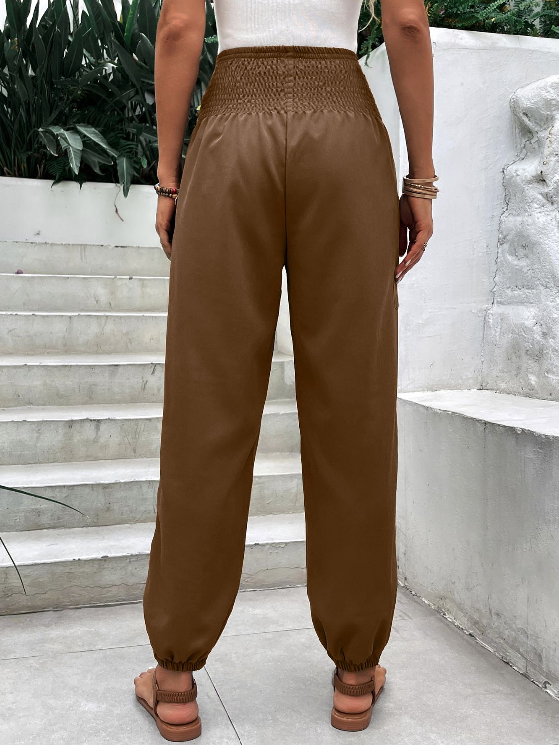 Brown relaxed-fit trousers with smocked waistline and cinched ankles.