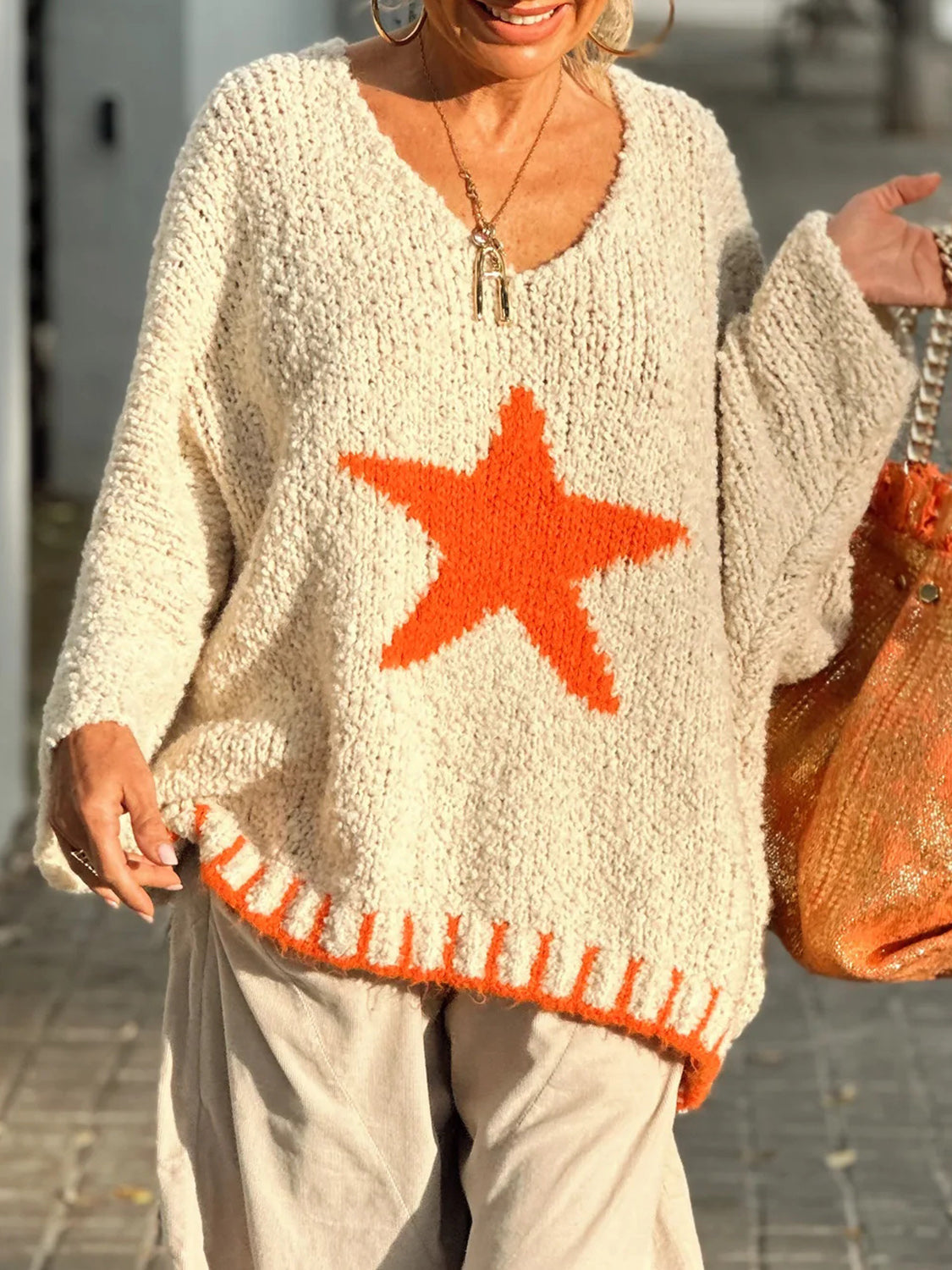 Cream knit v-neck sweater with orange star and striped hem.