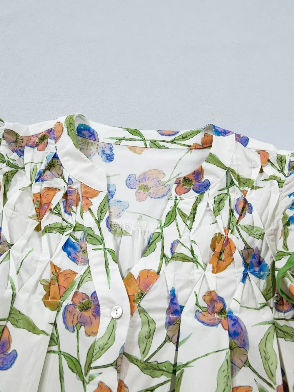 Cotton V-neck shirt with vibrant floral print, pleats, and button detail.