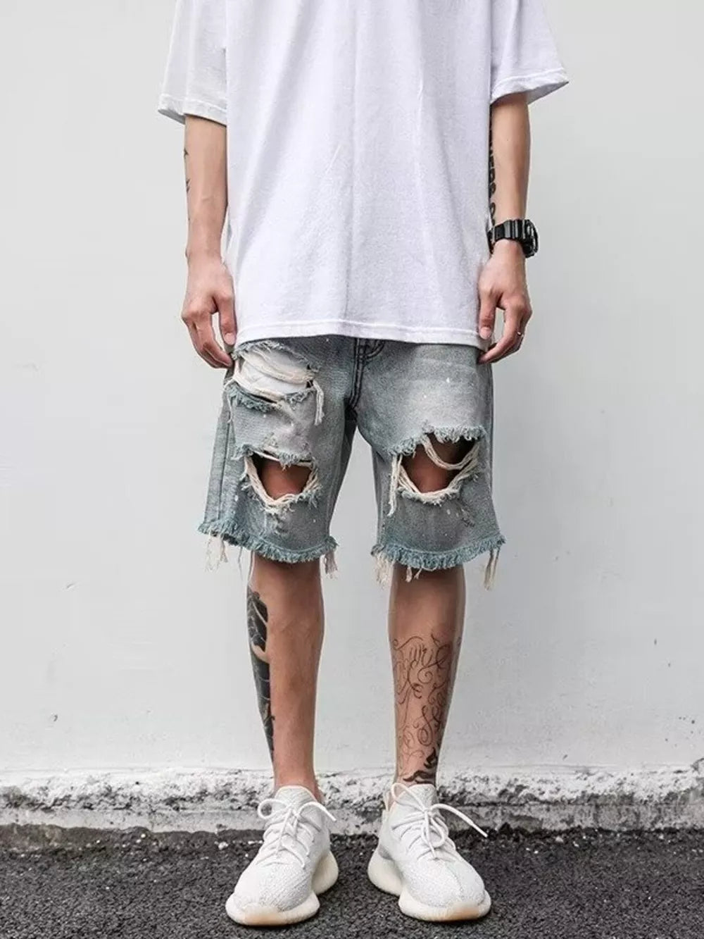 Men's light blue distressed denim shorts with raw hem and large rips.
