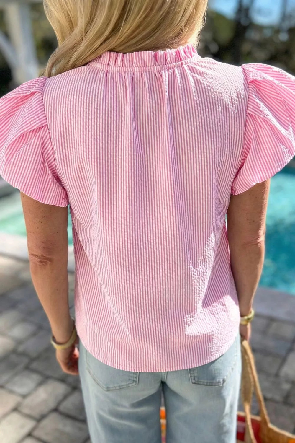 Pink seersucker blouse with textured stripes, ruffled neckline, and puff sleeves.