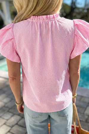Pink seersucker blouse with textured stripes, ruffled neckline, and puff sleeves.