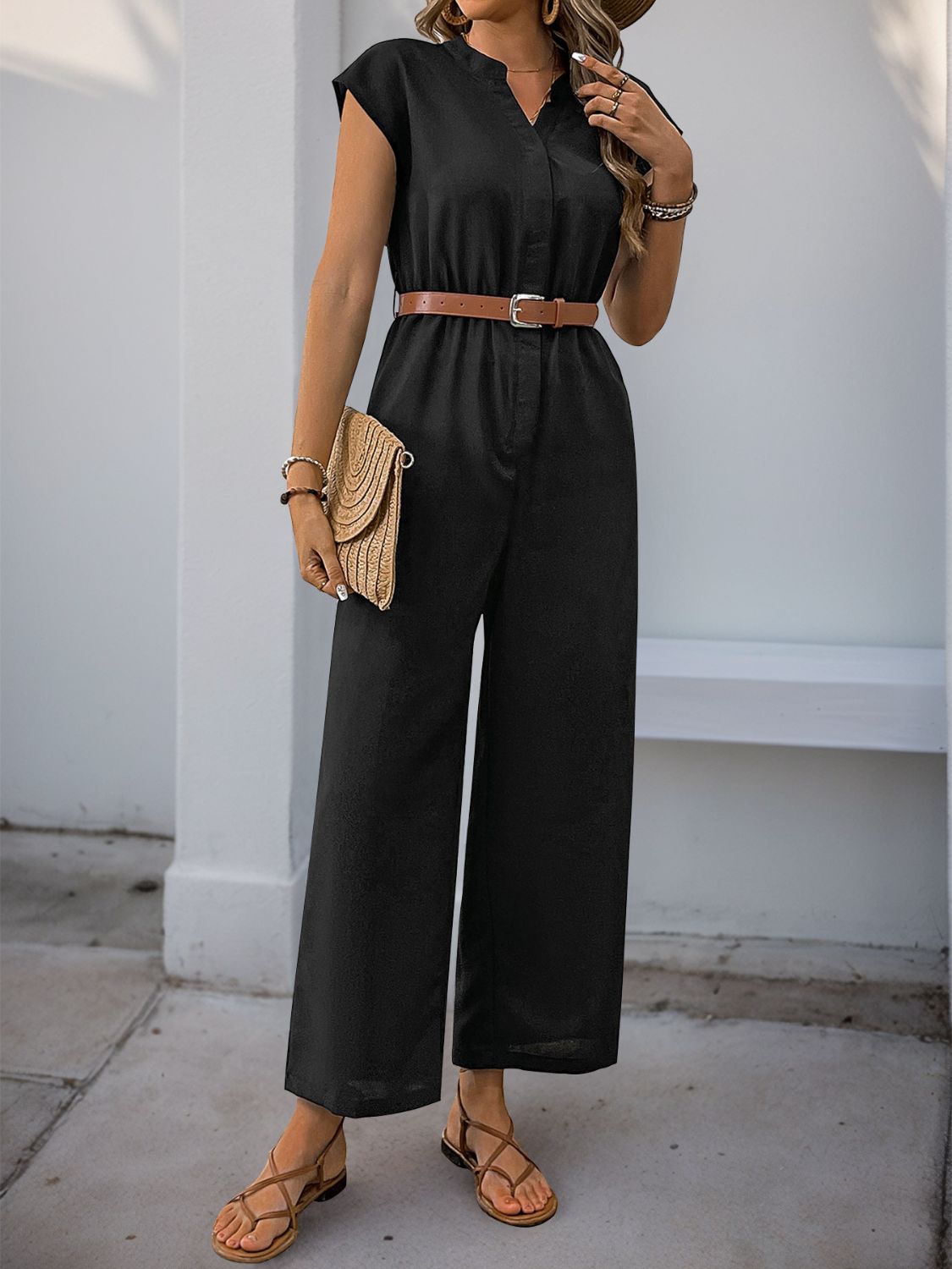 Black cap-sleeve button-down wide-leg jumpsuit with a brown belt and straw clutch.