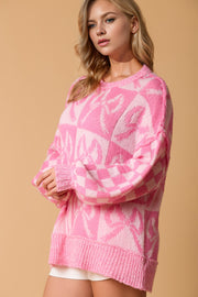 Pink knit sweater with checkered and abstract pattern, crew neck, long sleeves with bow detail.