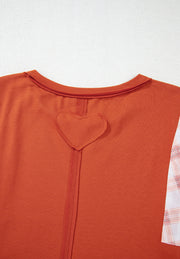 Orange-red blouse with heart detail on back and plaid patchwork sleeve.