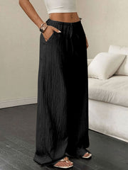 Black crinkled wide-leg drawstring pants with pockets, styled casually.