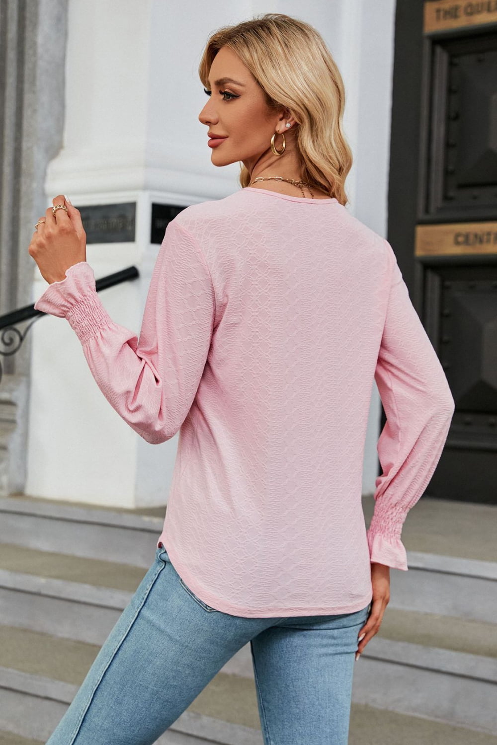 Blush pink textured V-neck blouse with smocked cuffs and lace trim.