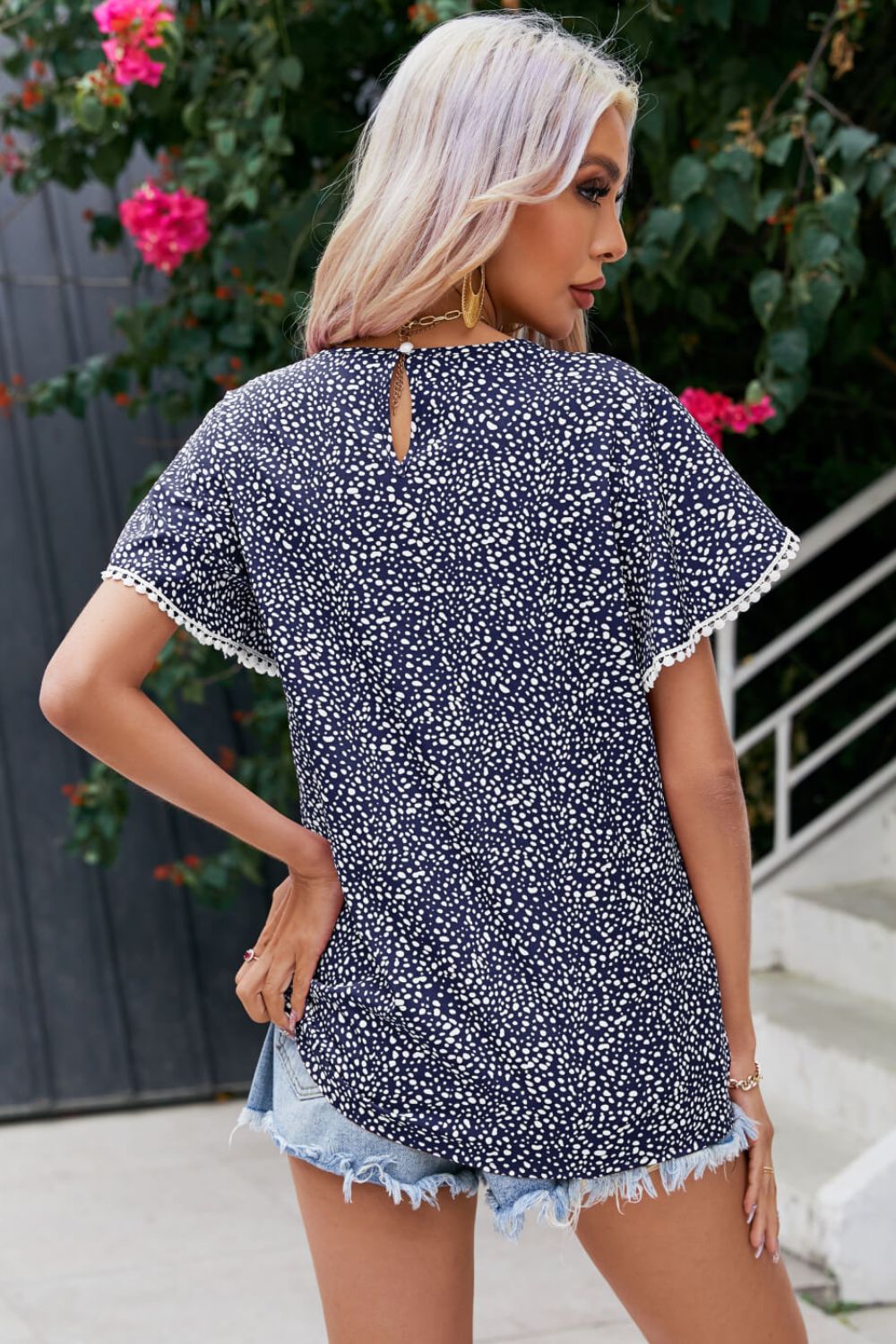 Dark blue dotted polyester blouse with flutter sleeves and pom-pom trim.