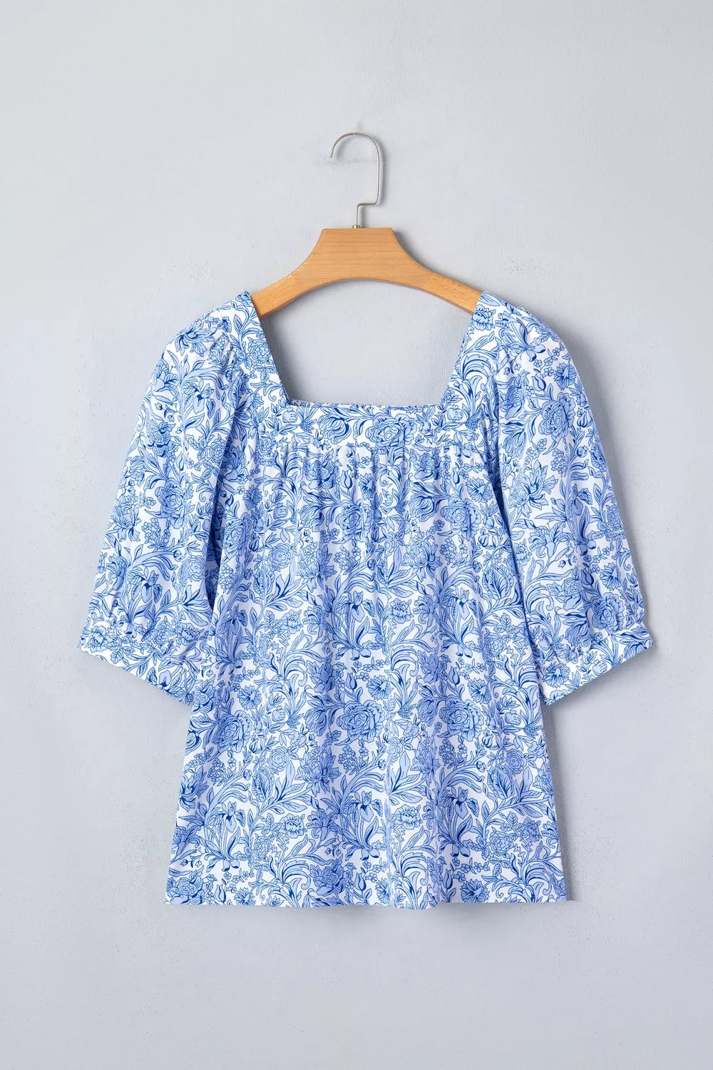Floral pleated blouse with square neckline and short sleeves in blue and white print.