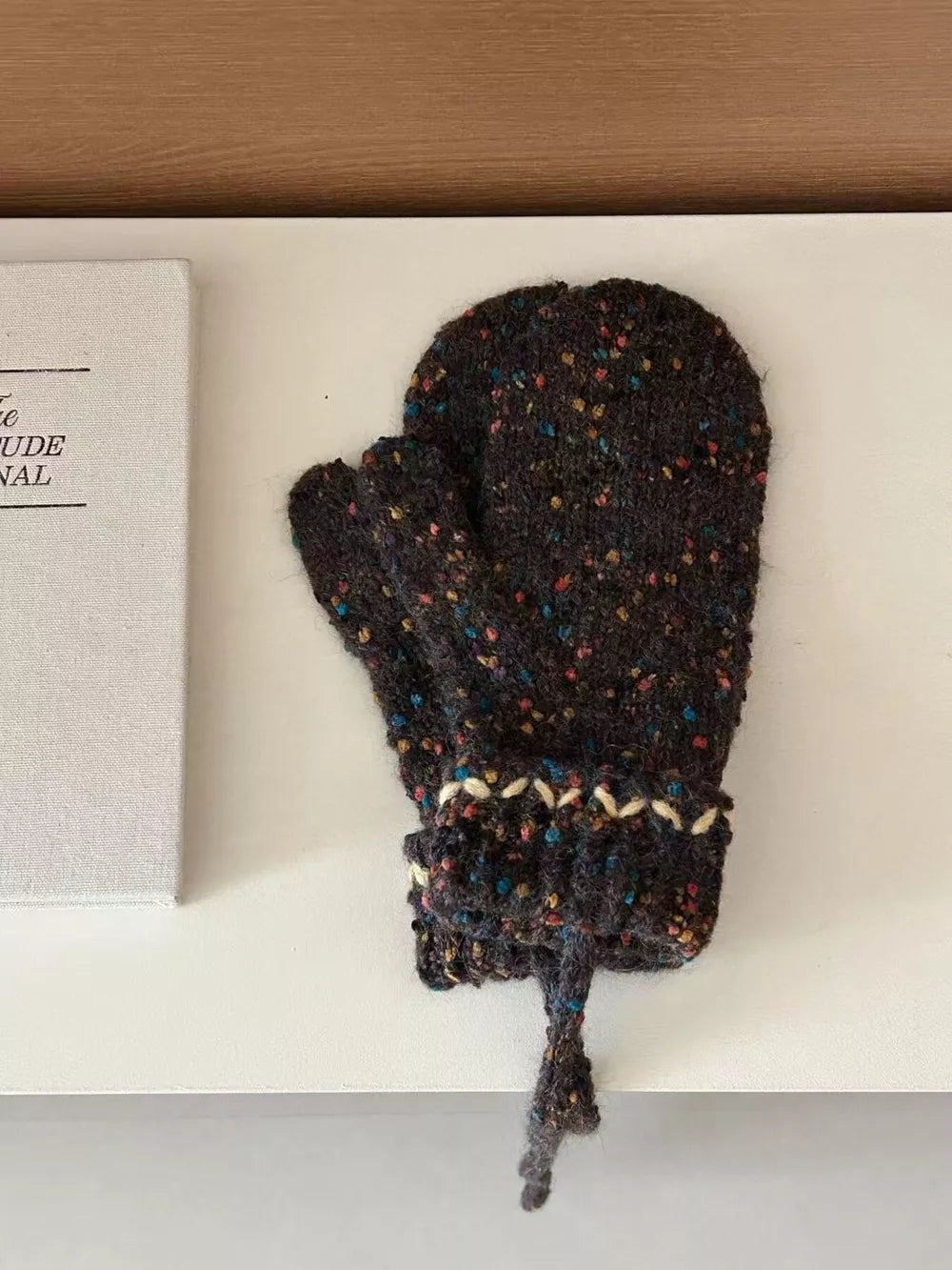 Textured brown knit mittens with zig-zag detail and pom-pom tie.