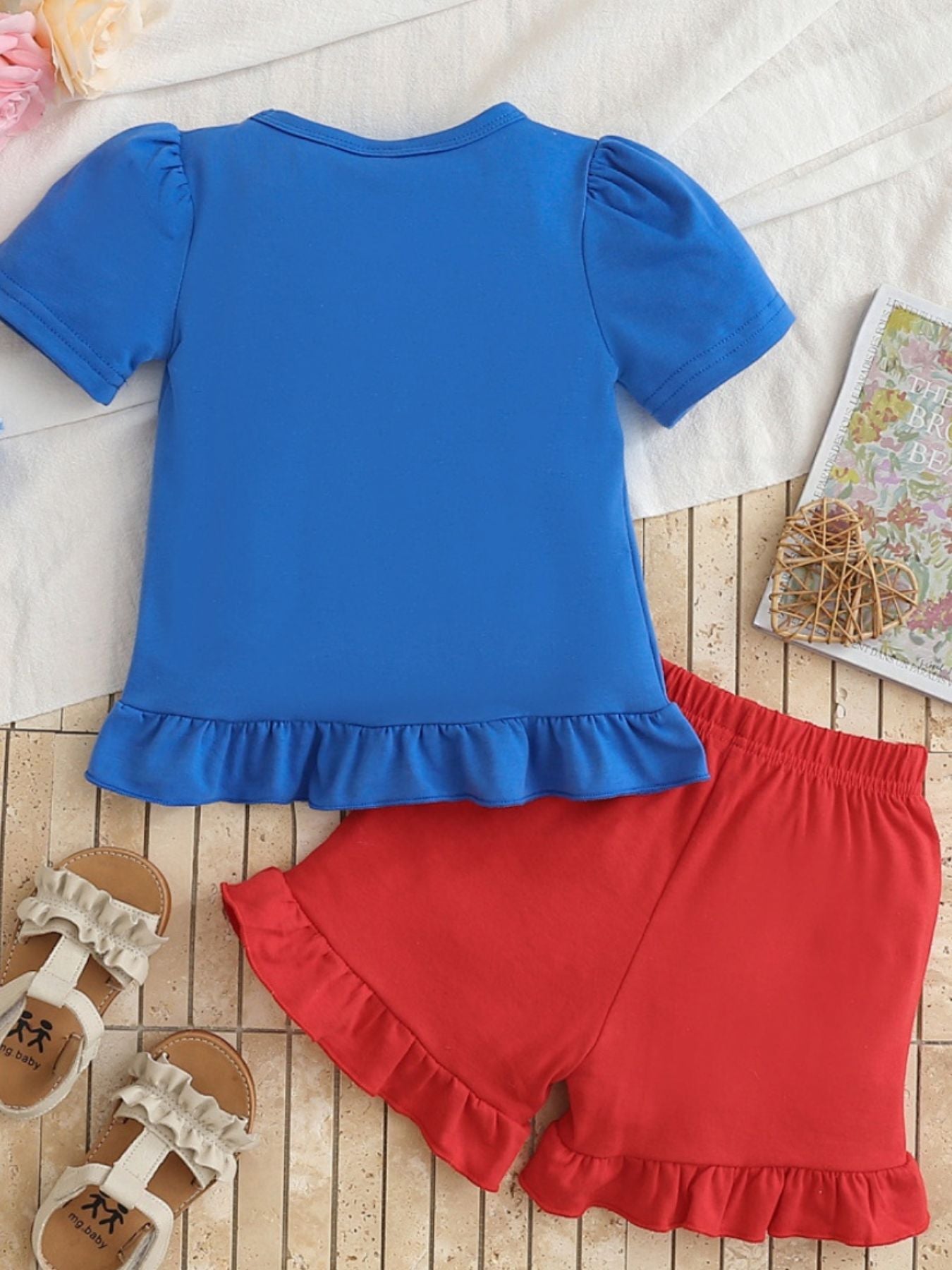 Children's blue short sleeve tee with ruffled hem and red ruffled shorts.
