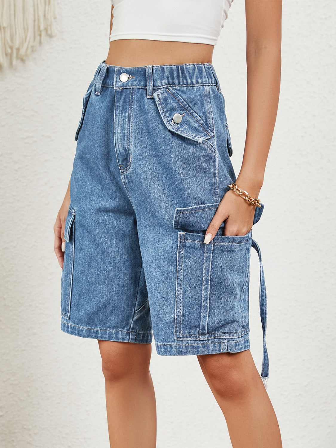 Medium wash denim Bermuda shorts with multiple cargo pockets and button details.