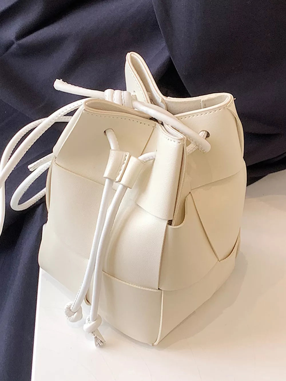 White woven mini bucket bag with drawstring closure and leather detail.