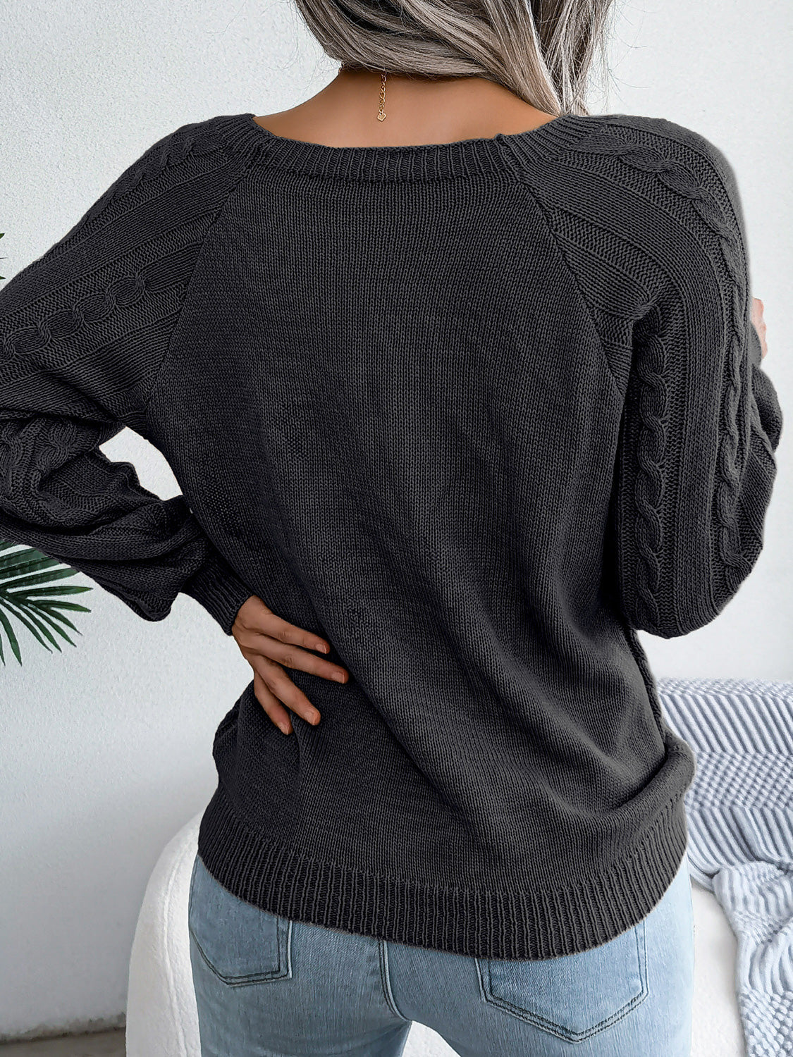 Charcoal cable-knit sweater with buttoned shoulder detail and raglan sleeves.