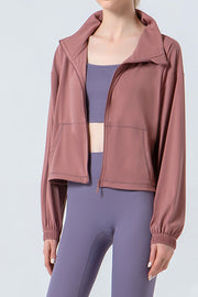 Dusty pink active jacket with gathered hemline and zip front, worn with a sports bra and leggings.