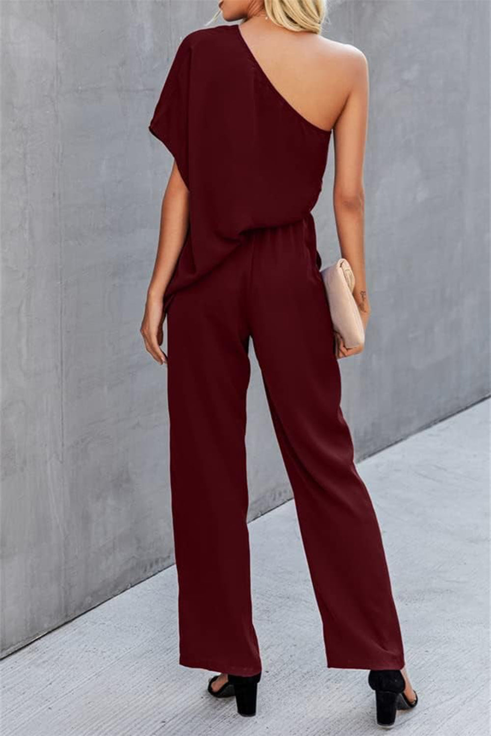 Burgundy asymmetric drape-sleeve wide-leg jumpsuit with cinched waist.