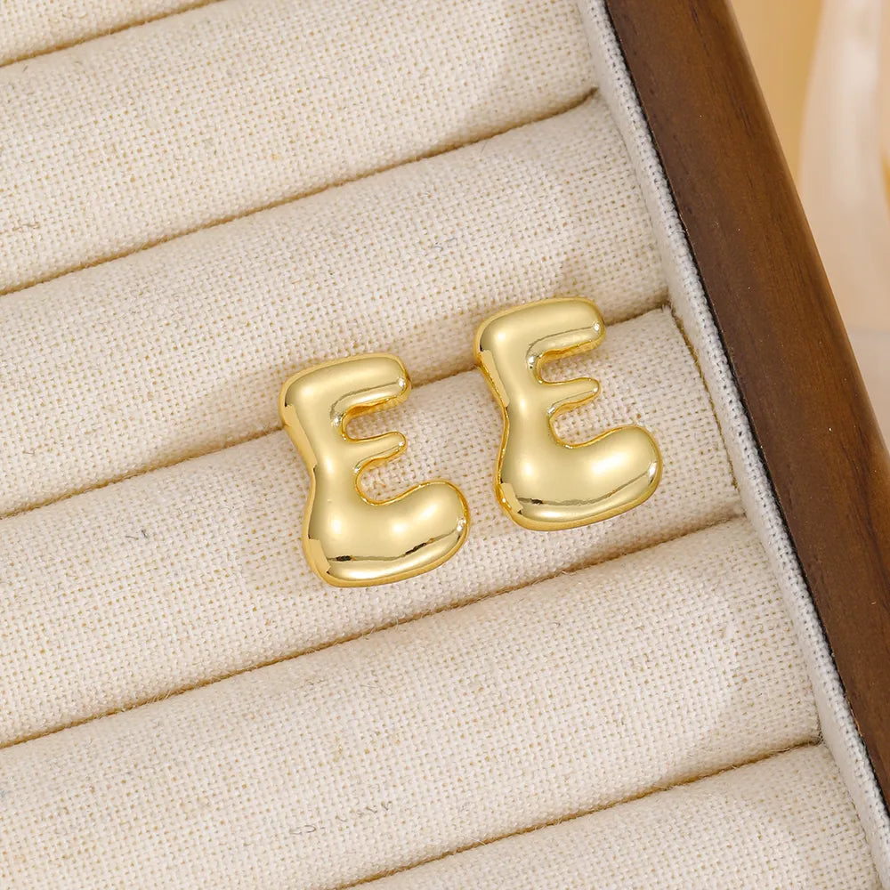 Alphabetical sculptural stud earrings in gold, featuring the letter E.