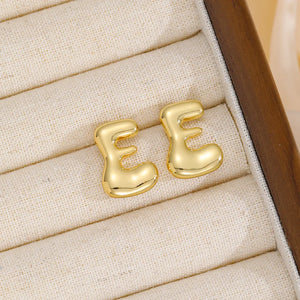 Alphabetical sculptural stud earrings in gold, featuring the letter E.